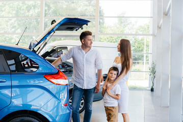 A happy young family chooses and buys a new car at a car dealership. Buying a new car