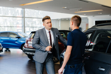 A young businessman with a salesman looks at a new car in a car dealership. Buying a car