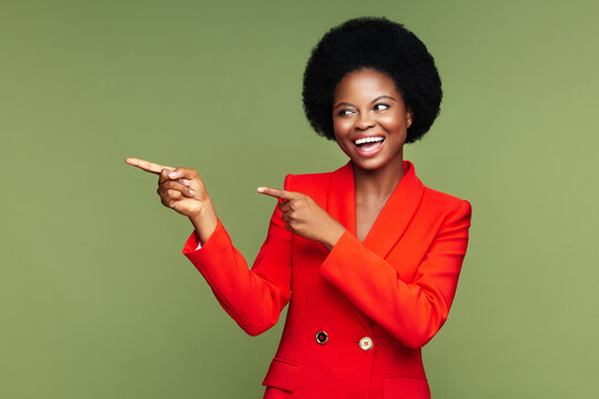 Joyful African Business Woman In Red Suit Point Finger Away Cheerful Indicate Space For Promo Or Ads. Young Afro American Female With Ethnic Hairstyle, Perfect Skin And Excited Toothy Smile Show Right