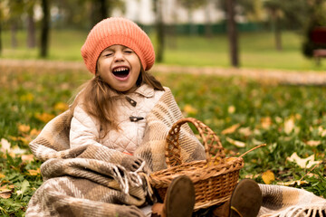 Little Cute Preschool Minor Girl In Orange Beret On Plaid At Yellow Fallen Leaves In Basket Laughs Wide Smiling Closed Eyes In Cold Weather In Fall Park. Childhood, Family, Motherhood, Autumn Concept