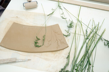 Close up ceramist hands imprinting herb on raw clay with rolling pin. Handmade, hobby art and...
