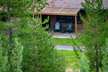 Fototapeta na wymiar View of cabin patio with Adirondack chairs, peeking through pine trees, rest and relaxation 