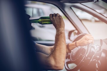 Man drives a car with a bottle of beer behind the wheel of a car.