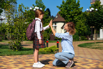 Back to school. Caucasian schoolgirl with backpack and uniform says goodbye to her smiling mother on the street before going to school.