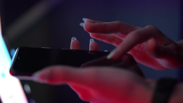 women's hands hold the phone and touch the screen in the neon lights.