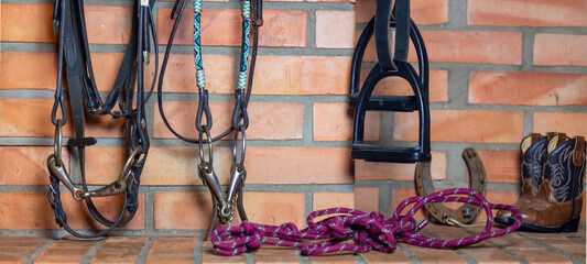 Horse riding equipment background. Horse riding hobby. . Halter, ropes, bit, bridle, stirrups hang on the brick wall of the stable.