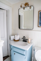 A small guest bathroom with a vintage blue vanity, retro black mirror, and clear glass light fixture in a recently renovated short term rental cottage