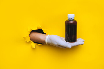 The hand of a doctor (pharmacist) in a white medical glove holds an empty dark brown jar of...
