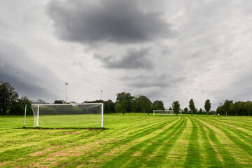 Obraz premium White metal soccer or football goal post and freshly cut training pitch. Cloudy sky. Simple sport background. Nobody. Cut green grass on a field.