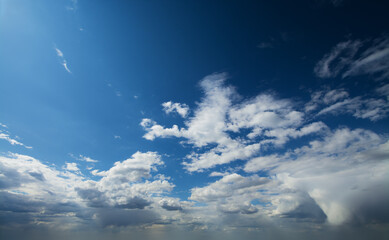 Fototapeta premium White fluffy clouds moving softly across blue sky in bright sunshine with dense overcast on the background.
