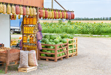 Roadside farmers market selling organic eco foodstuffs against the background of a field with sunflowers. Vegetable oil in bottles, potatoes in nets, watermelons, pumpkin, nuts on the counter.