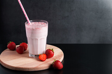 Milkshake with strawberries on black background. Summer drink in a glass with a paper straw.