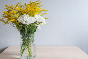 Autumn bouquet of flowers from white chrysanthemums, yellow mimosa, in a glass vase on the table.
