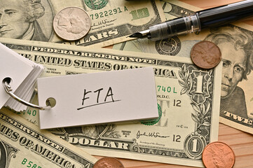 On top of the dollar bills on the table, there is a word book with the financial term FTA written...