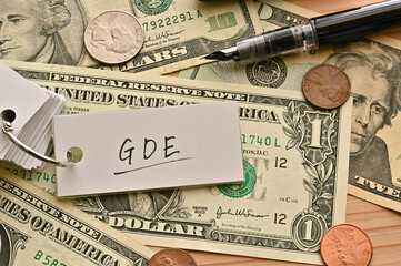 On top of the dollar bills on the table, there is a word book with the financial term GDE written on it. It is an abbreviation for gross domestic expenditure.