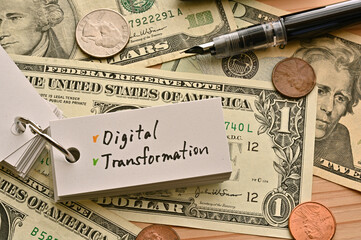 On top of the dollar bills on the table, there is a word book with the financial term Digital Transformation written on it.