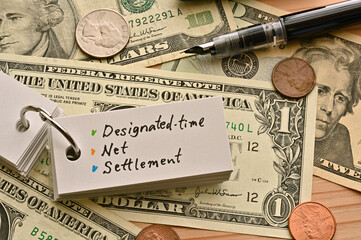 On top of the dollar bills on the table, there is a word book with the financial term designated-time net settlement written on it.