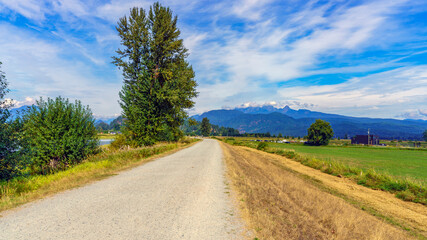 Fototapeta na wymiar Popular biking/hiking trail alongside Alouette River near Pitt Meadows, BC, with farmland to right and mountains in background