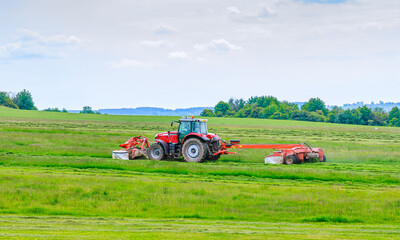 Obraz premium A red tractor mows the grass on a farmer's field. Two mowers will mow a large area of the field.
