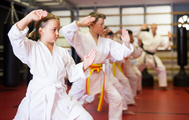 Young boys and girls in kimono doing kata moves with their trainer in gym. © JackF