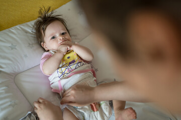 Top view on caucasian baby lying on the bed while her mother is changing diapers and clothes four...