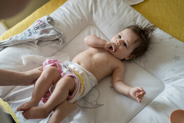 Top view on caucasian baby lying on the bed while her mother is changing diapers and clothes four months old daughter at home - parenting childhood new life and growing up concept