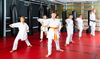 Group of preteen boys and girls doing karate kicks with male coach during karate class © JackF