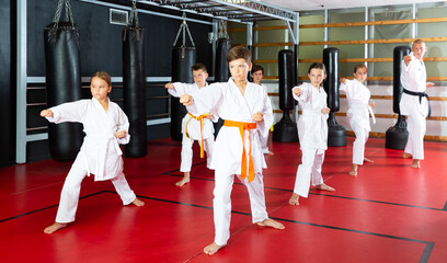 Group of preteen boys and girls doing karate kicks with male coach during karate class