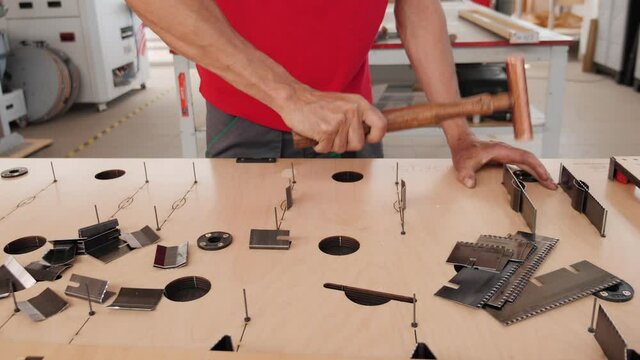 Manufacturing professional die cutter plate - worker hands inserting cutting blades in plywood plank slots fastening with copper head hammer, camera slide