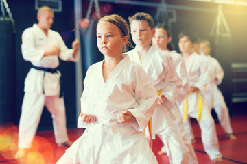 Kids in kimonos practicing effective karate techniques in group workout at training room