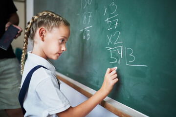 Spanish school kid making exercise on chalkboard in front of teacher