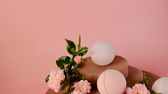 Bath bombs with rose extract.Pink bath bombs and pink rose flowers on burgundy pedestal on a light pink background.Organic vegan eco cosmetics. Organic natural cosmetics with rose extract.Flower Bath