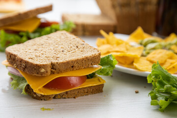 sandwiches prepared with the fresh ingredients of whole wheat bread, cheese, lettuce and a plate with nachos on a table, delicious food prepared at home, snack