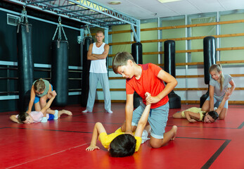 Sportive preteen kids practicing in pair self-protection in class with teacher