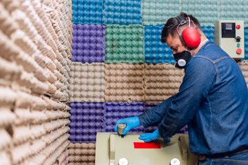 Male industrial worker with protective mask and hearing protectors closing the lid of a material testing machine