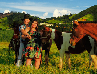 Beautiful western country couple stading next to majestic brown horses in front of a wonderful...