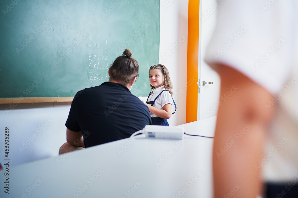 Wall mural Spanish teacher wearing mask shows to student girl how to make exercise