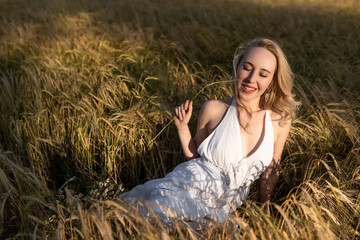 Beautiful young blonde in a wheat field in a white dress in summer 