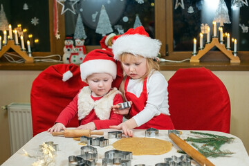 Two cute little sisters are cooking Christmas cookies in cozy home kitchen.
