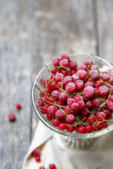 Frozen red currants in a glass vase on a cloth on a rustic wooden table. Close-up.