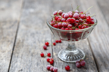 Frozen red currants in a glass vase on a rustic wooden table. Close-up.