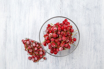 Frozen red currants in a glass vase on a white wooden table. Close-up.