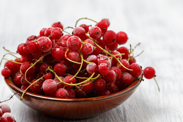 Frozen red currants in a brown ceramic vase on a white wooden table. Close-up.