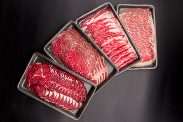 Group of mix raw beef. Sliced raw beef place in a row on a black plastic tray isolated on a black...