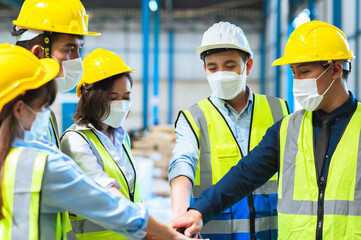 Factory employee of engineers, foreman technicians and staff. Wear a mask hard hat and vest. Standing in a circle, holding hands together Joining forces to create success in the organization. Teamwork