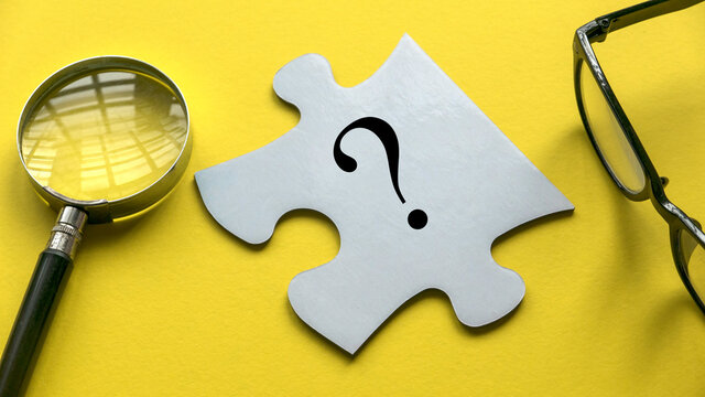 Questions symbol on a white piece of jigsaw puzzle together with glasses and magnifying glass on a yellow background.