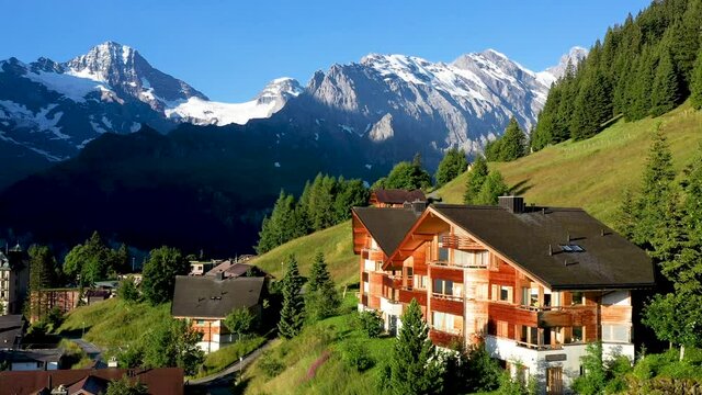 Cinematic drone shot of Murren, a traditional Walser mountain village in the Bernese Highlands of Switzerland. Flying over homes and hotels with mountains in the distance