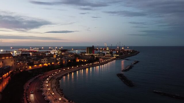 Cinematic drone shot during sunset in Italian shore, city lights and sea.