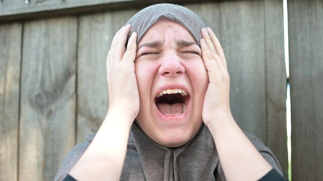 a teenage refugee girl is crying and screaming, holding her head in her hands, screaming in pain.