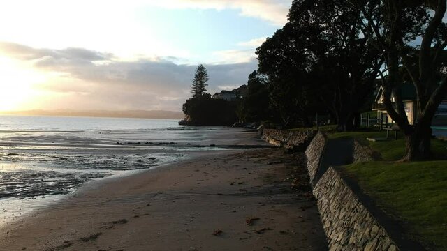 Drone flying slowing along a beach retaining wall at sunrise.